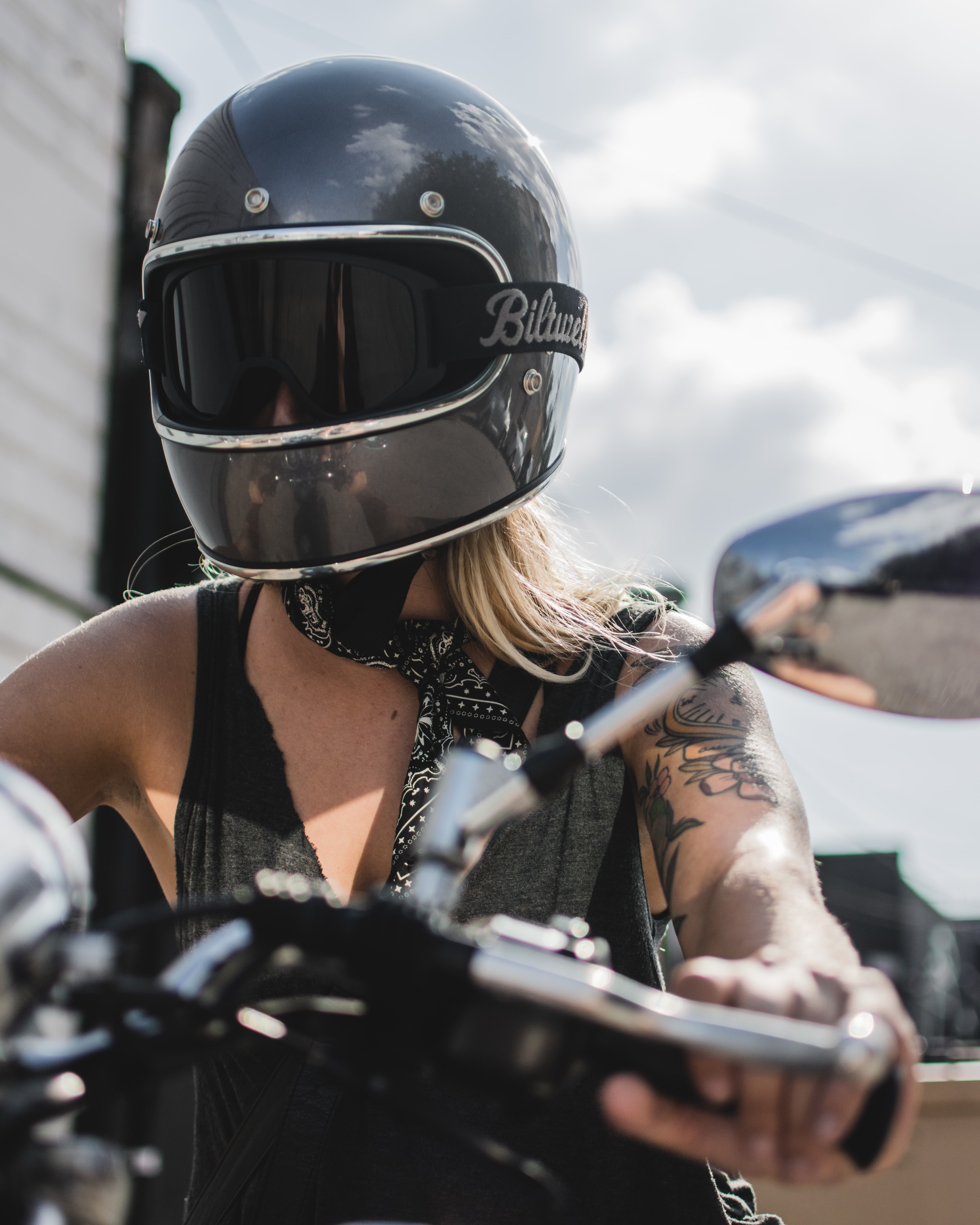 blonde woman with tattoo wearing a dark grey helmet riding a motorcycle 