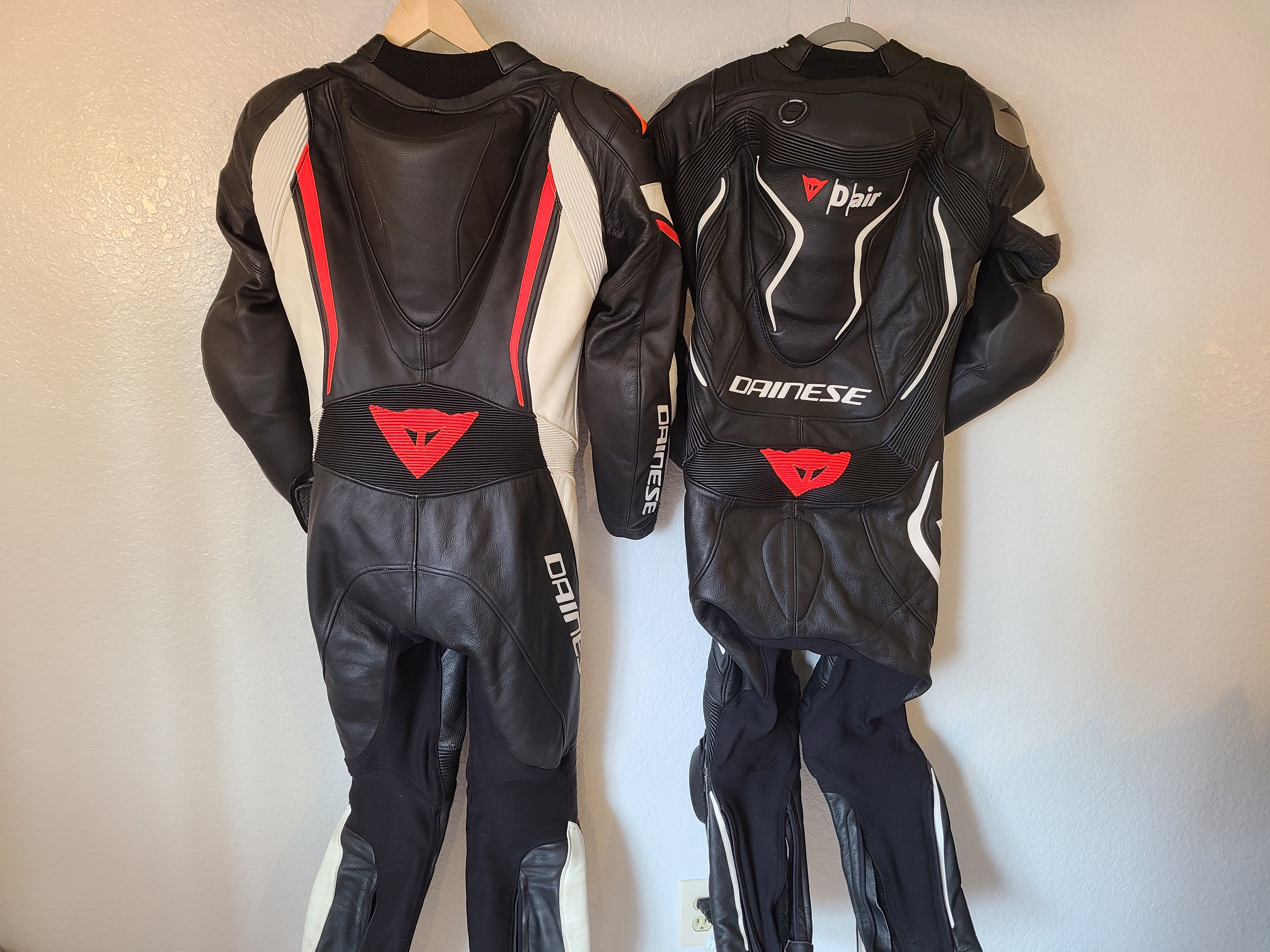 2 black, red, and white motorcycle race suits hanging next to each other