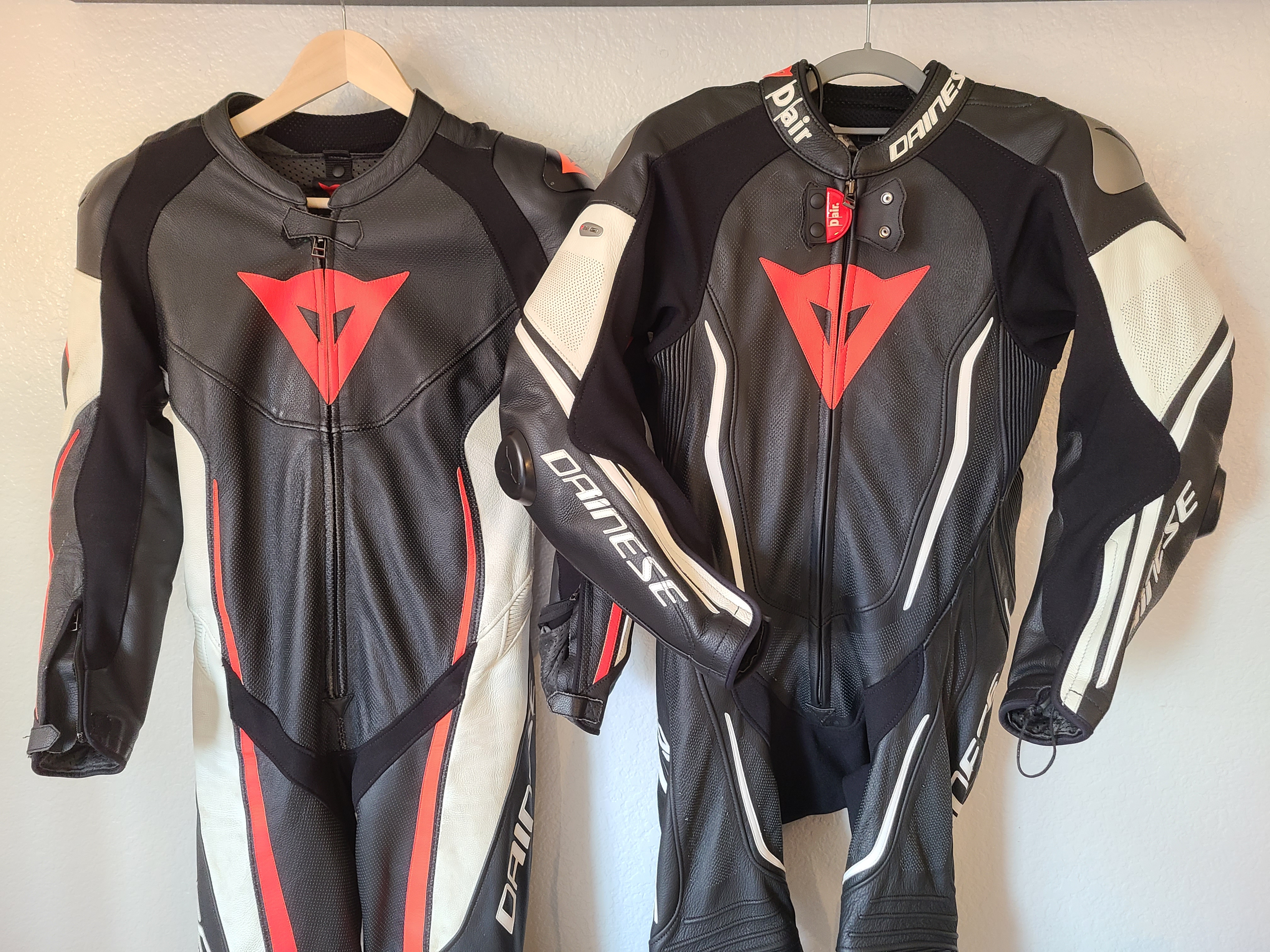 Two black, red, and white leather motorcycle race suits hanging side by side